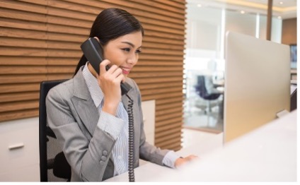 Woman in business clothes sitting at a desk answering the phone.