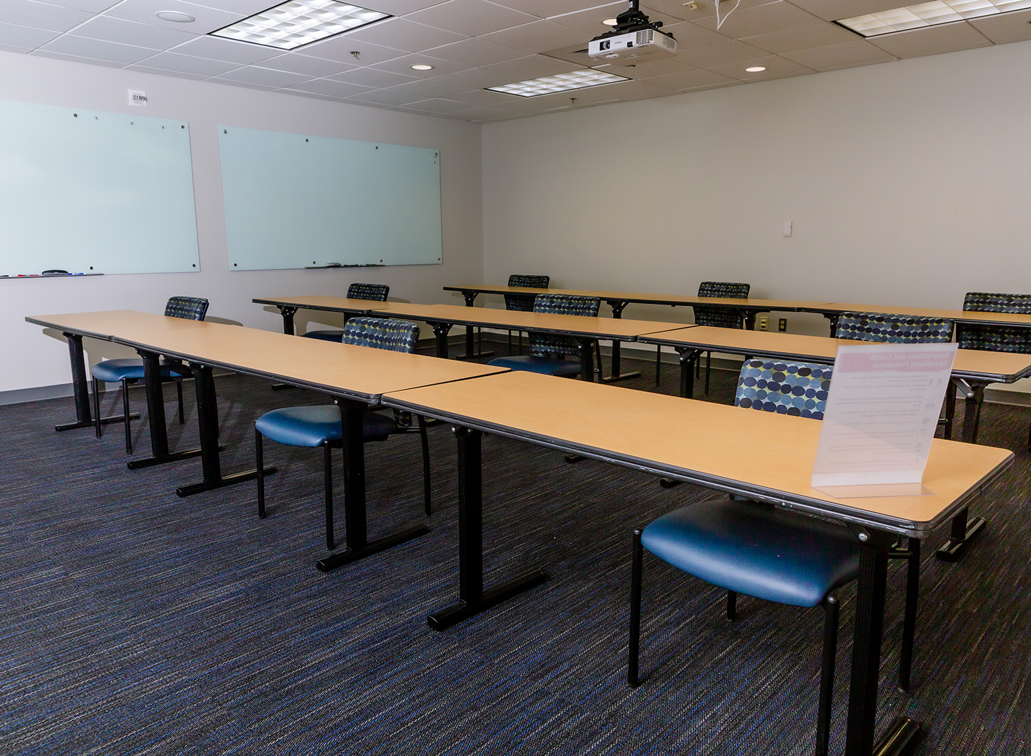 Meeting Room 302 facing the back of the room showcasing long tables and spaced seating along with two white boards