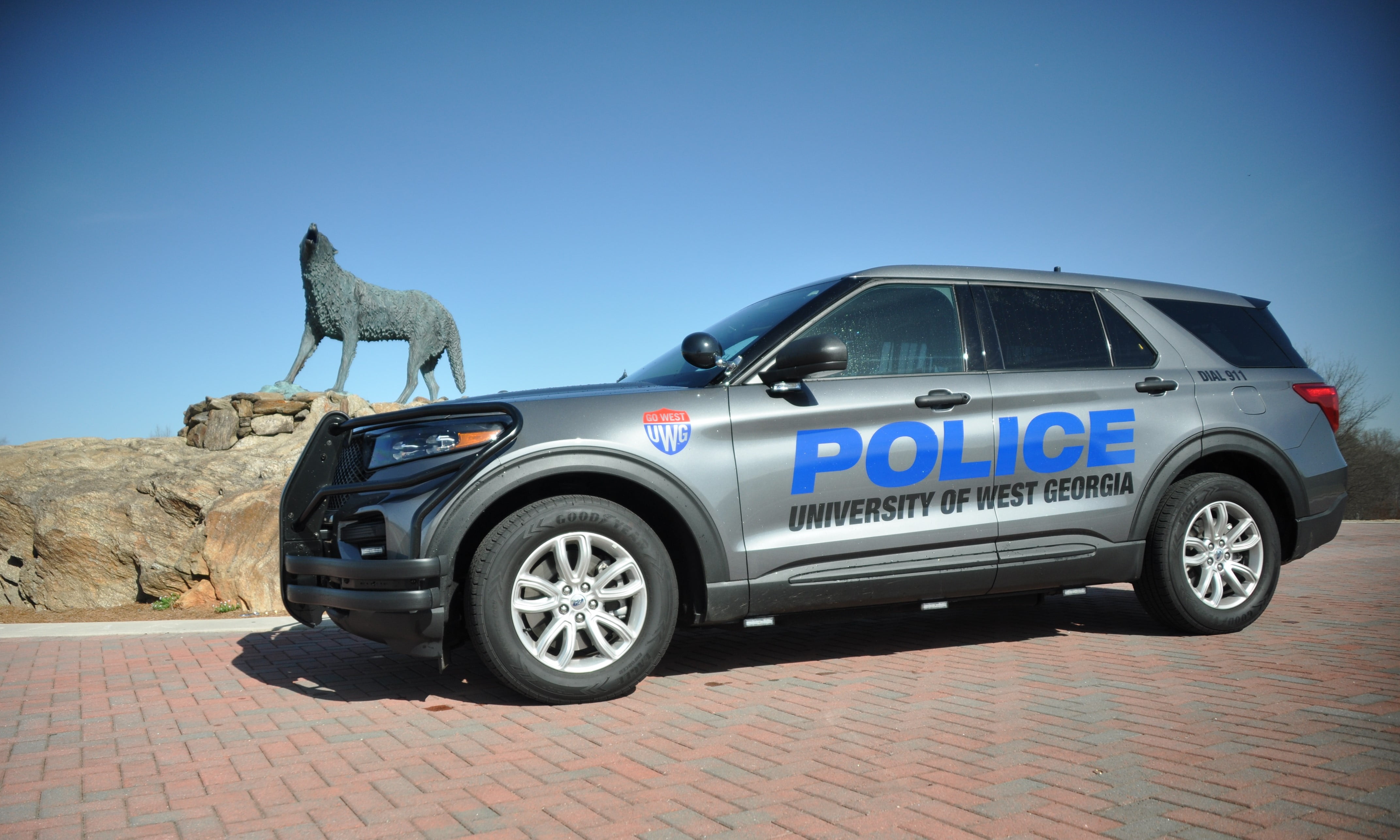 Dark grey police vehicle parked at wolf plaza with the wolf statue positioned behind.